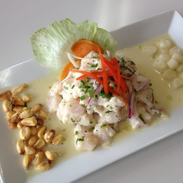Peruvian ceviche with white fish, red onions, chives, corn, and sweet potato on a white plate.