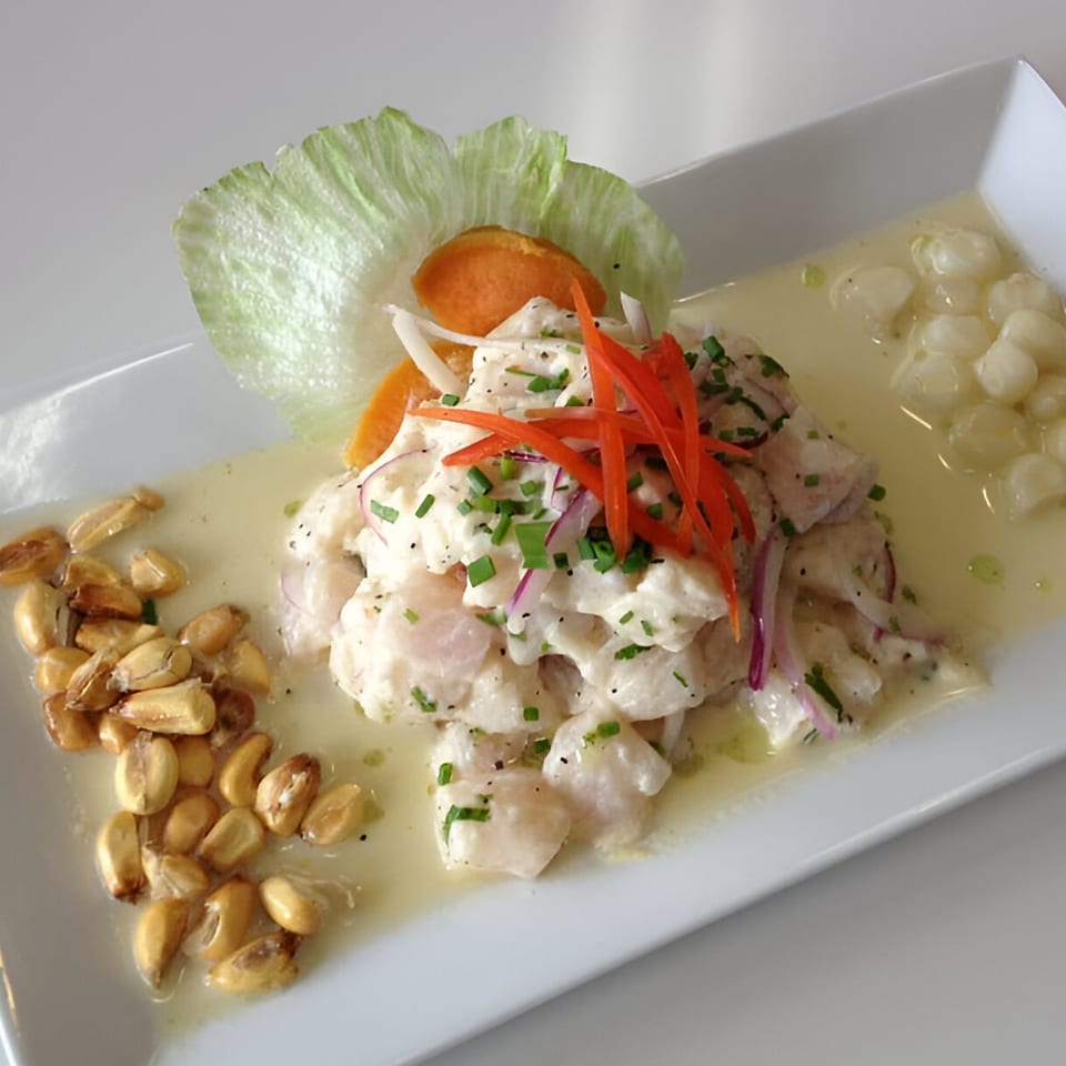 Peruvian ceviche with white fish, red onions, chives, corn, and sweet potato on a white plate.