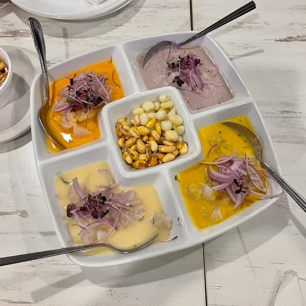 Peruvian ceviche sampler with various sauces, red onions, and corn in a white segmented dish.