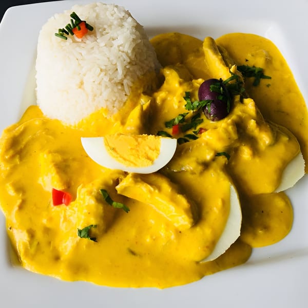 Peruvian Aji de Gallina with rice, hard-boiled egg, olives, and red pepper on a white plate.