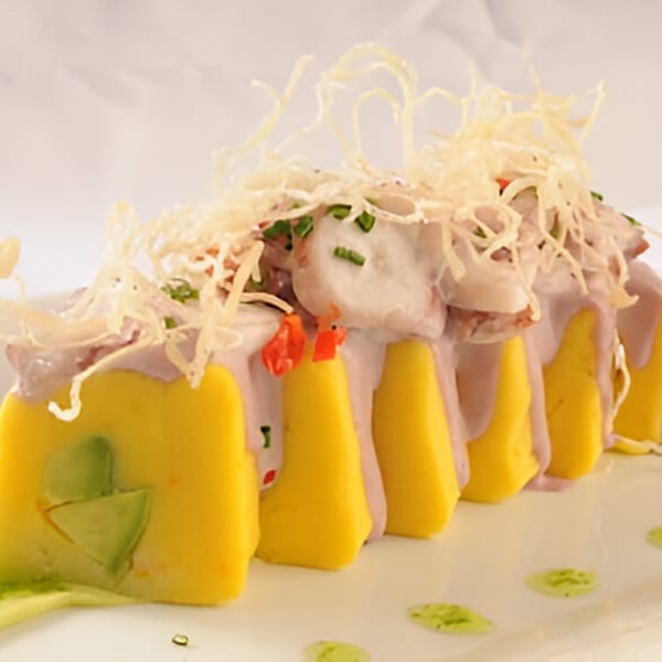 Peruvian causa dish with yellow potato base, creamy purple topping, and crispy garnish on a white plate.